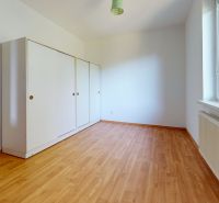 A room with a white wardrobe, a large window, and a wooden decor floor in a family house.