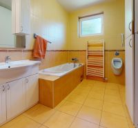 A bathroom in a family house with a bathtub, a sink, a window, and a tiled floor.