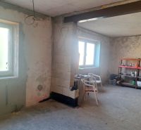 The interior of a family house with unfinished walls and windows, with a shelf and chairs.