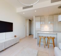 Living room in a two-room apartment with a television, kitchen, and bar stools.