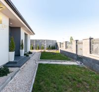 A family house in Bajč with a landscaped garden, a hedge, and a stone pathway.