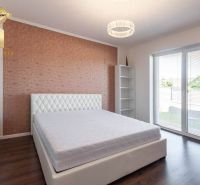 Bedroom in a family house with a double bed, wooden decor flooring, light wallpaper.