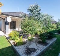 A family house in Bajč with a landscaped garden and a satellite dish.