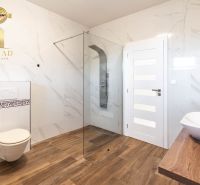 A bathroom with a glass shower enclosure, toilet, and wooden decor flooring in a family house.