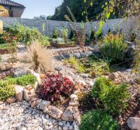 A garden with a pond in the exterior of a family house in Bajč, surrounded by greenery and stones.