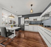 The kitchen of a two-room apartment with white furniture and a floor with a wood decor.