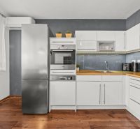A kitchen with white cabinets and a wood-patterned floor in a two-room apartment.