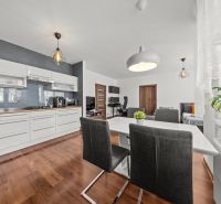 Living room of a two-room apartment with a kitchen, dining table, and wooden decor flooring.