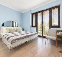 A bedroom in a family house with a wood-patterned floor and large windows.