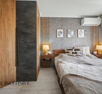 Bedroom in a three-room apartment with a wooden decor floor, a bed, and decorative paintings.