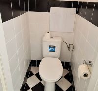 A toilet in a 2-room apartment with black and white tiles on the wall and floor.