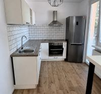 A kitchen in a 2-room apartment with appliances and a wooden decor floor.