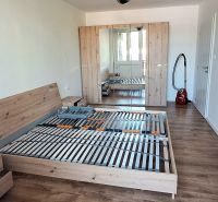 A bedroom in a two-room apartment with a wooden-decor floor, a bed, and a wardrobe.