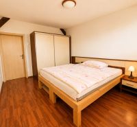A bedroom in a three-room apartment with a wood-patterned floor, a large wardrobe, and a light-colored bed.