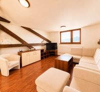 A bright living room with wood-patterned flooring, a corner sofa, and wooden beams.
