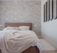 Bedroom in a family house with a patterned wall and mirrors, bed with a cream bedspread.