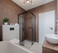 A family house bathroom with brown tiles, a shower corner, and a washbasin on a wooden decor.