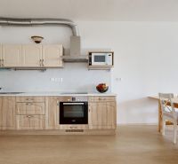 A kitchen in a 2-room apartment with appliances and a dining table on a floor with a wooden decor.
