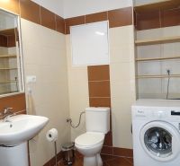 A bathroom in a 2-room apartment with a washing machine, sink, and shelves.