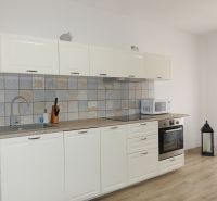 A kitchen unit in a 2-room apartment with a wooden decor floor, white furniture, and a built-in stove.