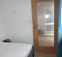 Bedroom in a 2-room apartment with a bed, glass doors, and curtains.
