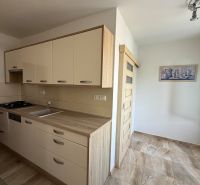 The kitchen of a 3-room apartment with a wooden decor floor and a light-colored kitchen unit.