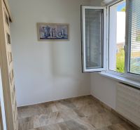 A room in a 3-room apartment with an open window, a light wall, and stone-design tiles.
