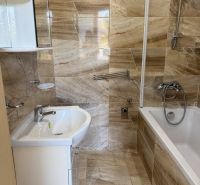 A bathroom with a bathtub and a sink, tiled with a brown marble decor in a 3-room apartment.