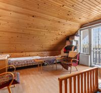Attic room in a family house with a wooden decor floor, comfortable armchairs, and a dining table.