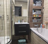 Bathroom with a bathtub, shower corner, and storage shelves in a 3-room apartment, floor with wood decor.