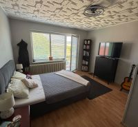 Bedroom in a family house with a wood-patterned floor, a bed, and a guitar.