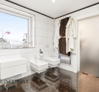 A bathroom in a family house with white tiles, modern fixtures, and plants on the windowsill.