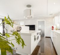 A kitchen in a family house with white cabinets and a plant, floor with wood decor.