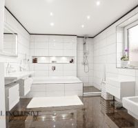 White bathroom with a bathtub and shower in a family house.