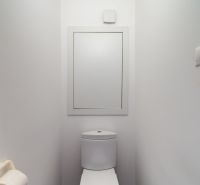 A toilet in a 4-room apartment with a wooden decor floor and white walls.