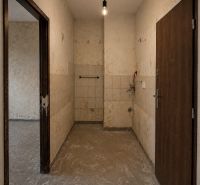 A spacious entrance area in a studio apartment with older tiles and lighting by a bulb.