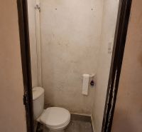 A toilet with prominent wall stains, gray floor, toilet paper holder.