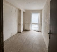 A view into an empty room in a two-room apartment with a concrete floor and balcony doors.
