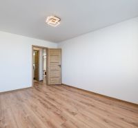 A room in a three-room apartment with a wooden decor floor and white walls.