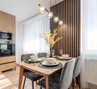 Dining table with four chairs in a three-room apartment, designer lighting, and a decorative wall.