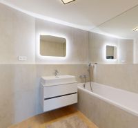 A bathroom in a 4-room apartment with a bathtub, backlit mirror, and washing machine.