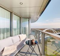 A balcony of a 4-room apartment with a sofa bed, a table, and a view of the Danube in Bratislava.