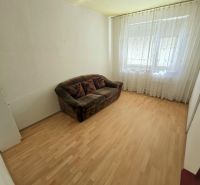 A room in a 3-room apartment with a sofa, wood-decorated flooring, and curtains.