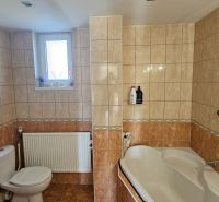 A bathroom in a family house with light tiles, a bathtub, and a window.