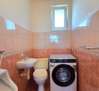 A bathroom in a family house with a washing machine, toilet, sink, and tiles in warm tones.