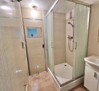 A bathroom with a corner shower in a 3-room apartment, a sink, and light tiles.