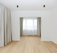 A room in a 3-room apartment with a wooden decor floor and large windows with curtains.
