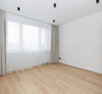 A room in a 3-bedroom apartment with a wooden decor floor and a large window with curtains.