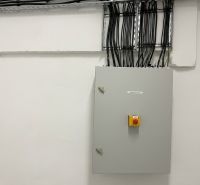 A distribution box in a warehouse and hall with numerous cables on the wall.