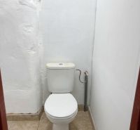 A toilet with white walls and ceramic tiles.